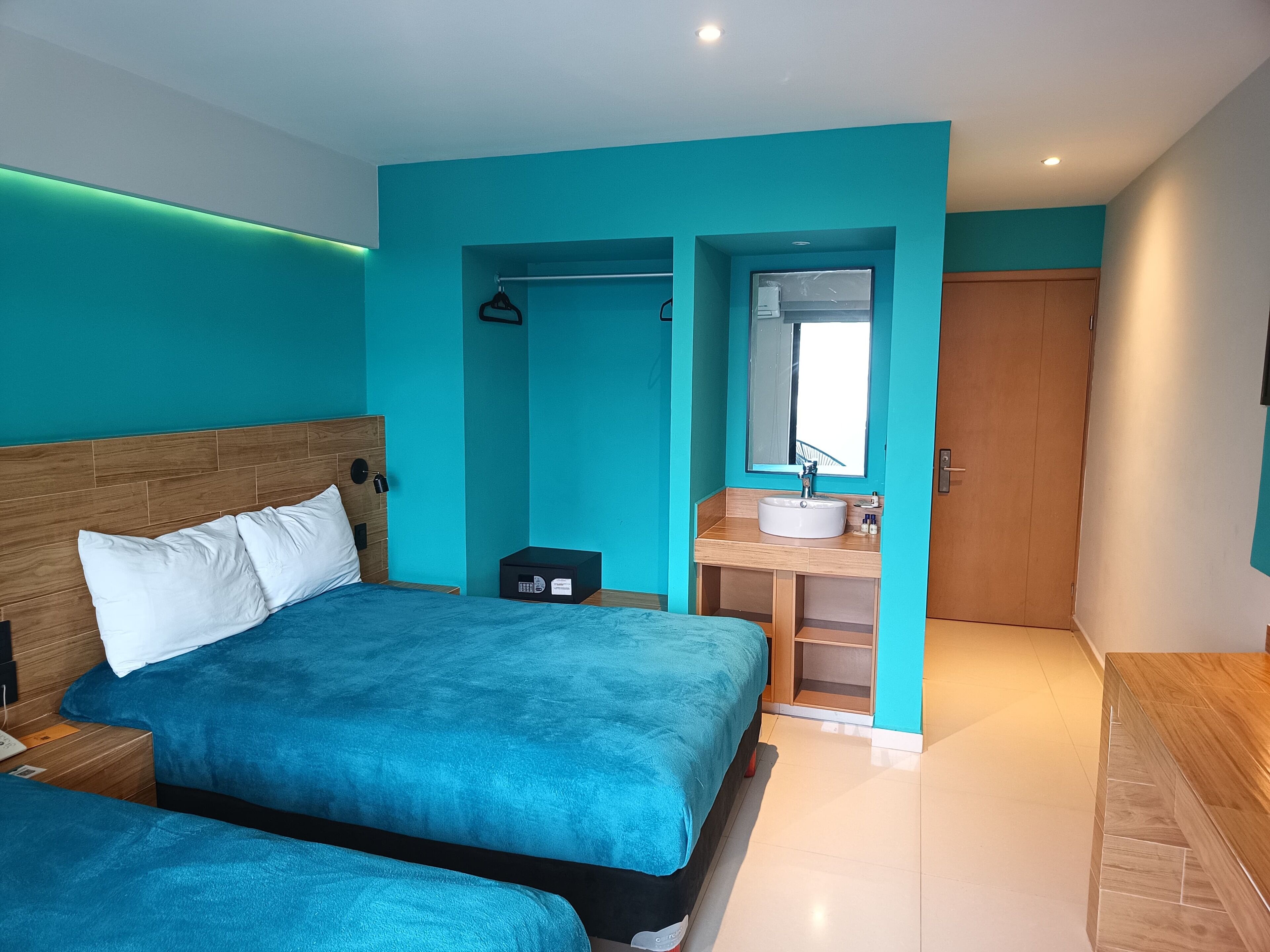 A modern bedroom with two beds, a bathroom with a sink and mirror, and a wooden wardrobe.