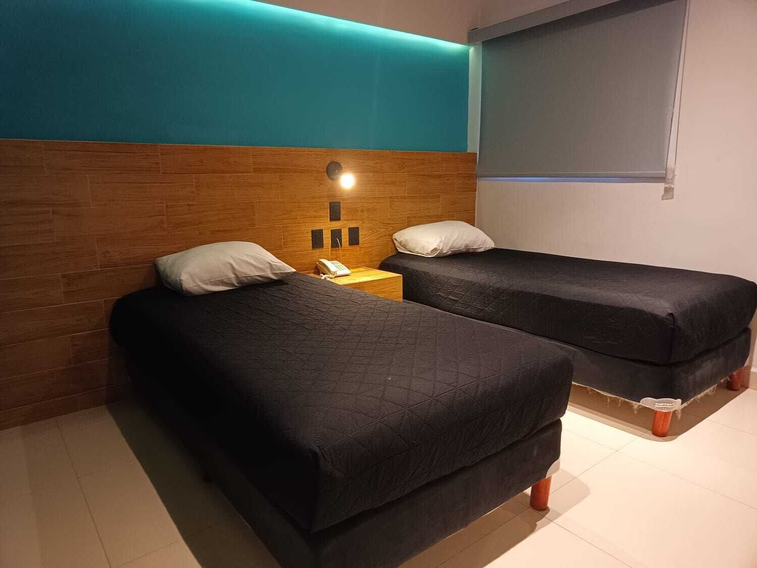 Ett hotellrum med två sängar, en sänggavel i trä, ett nattduksbord med en telefon och en väggmonterad TV.