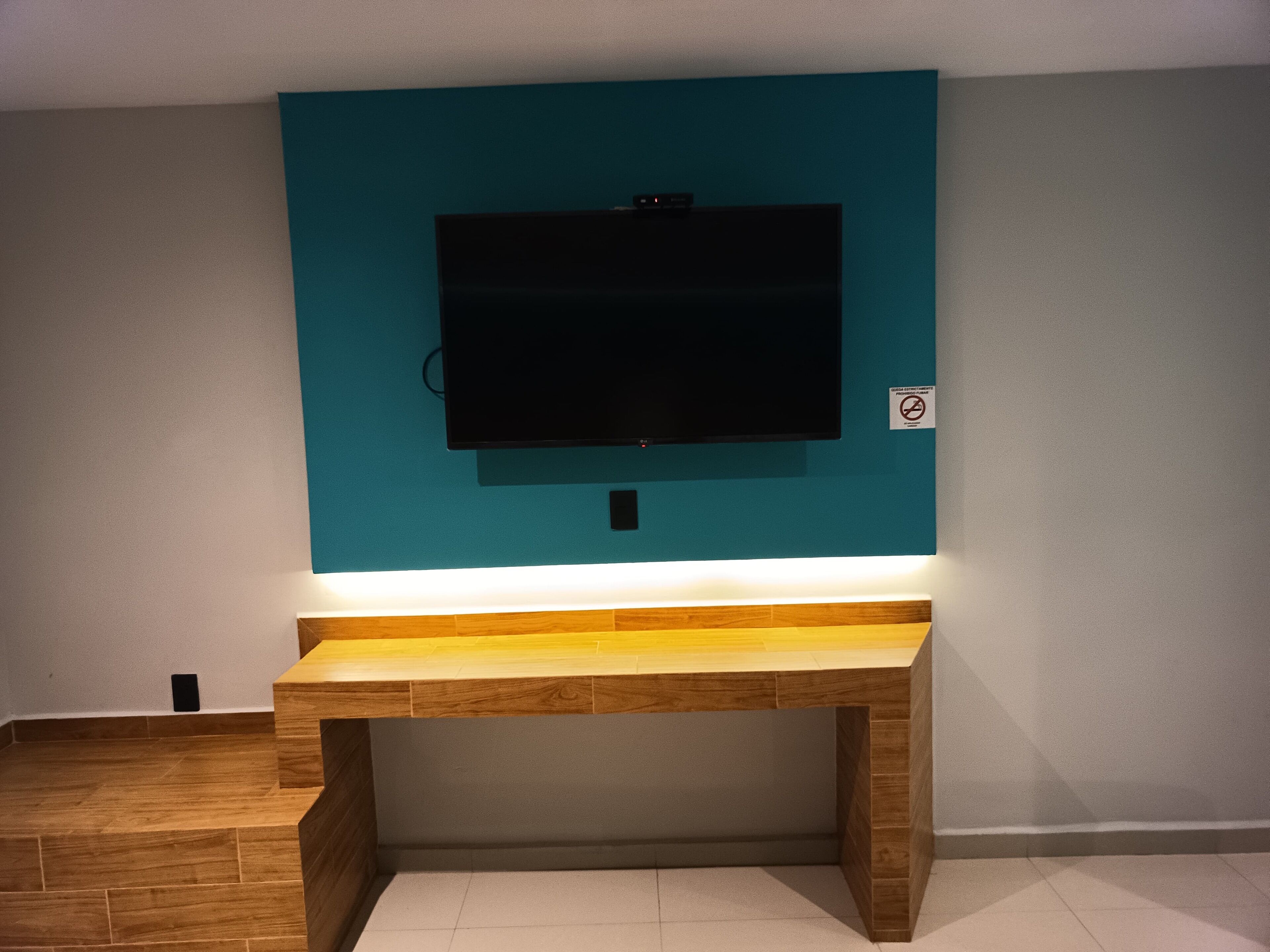 Una habitación con una pared verde azulado, un televisor de pantalla plana montado y un banco de madera.