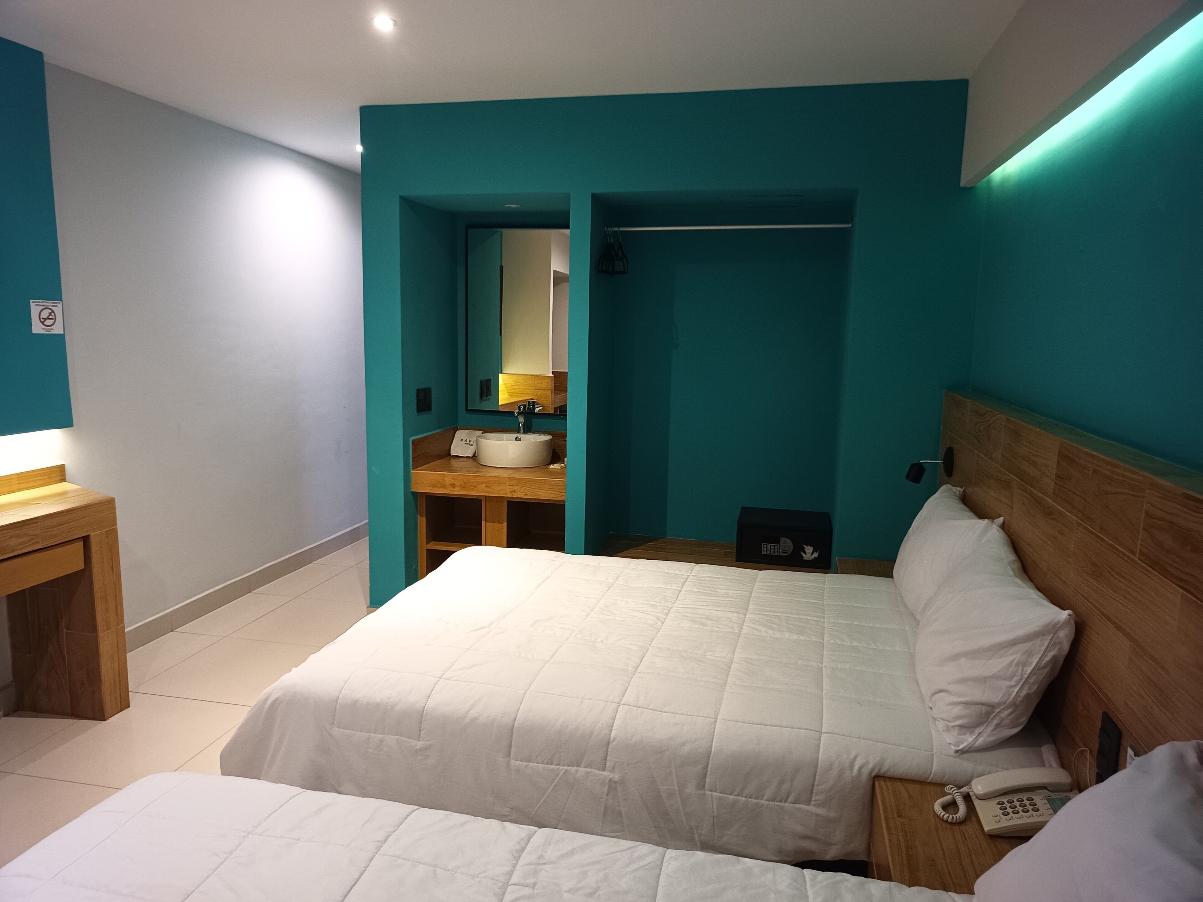 A hotel room with a bed, bedside table, and a bathroom with a sink and mirror.