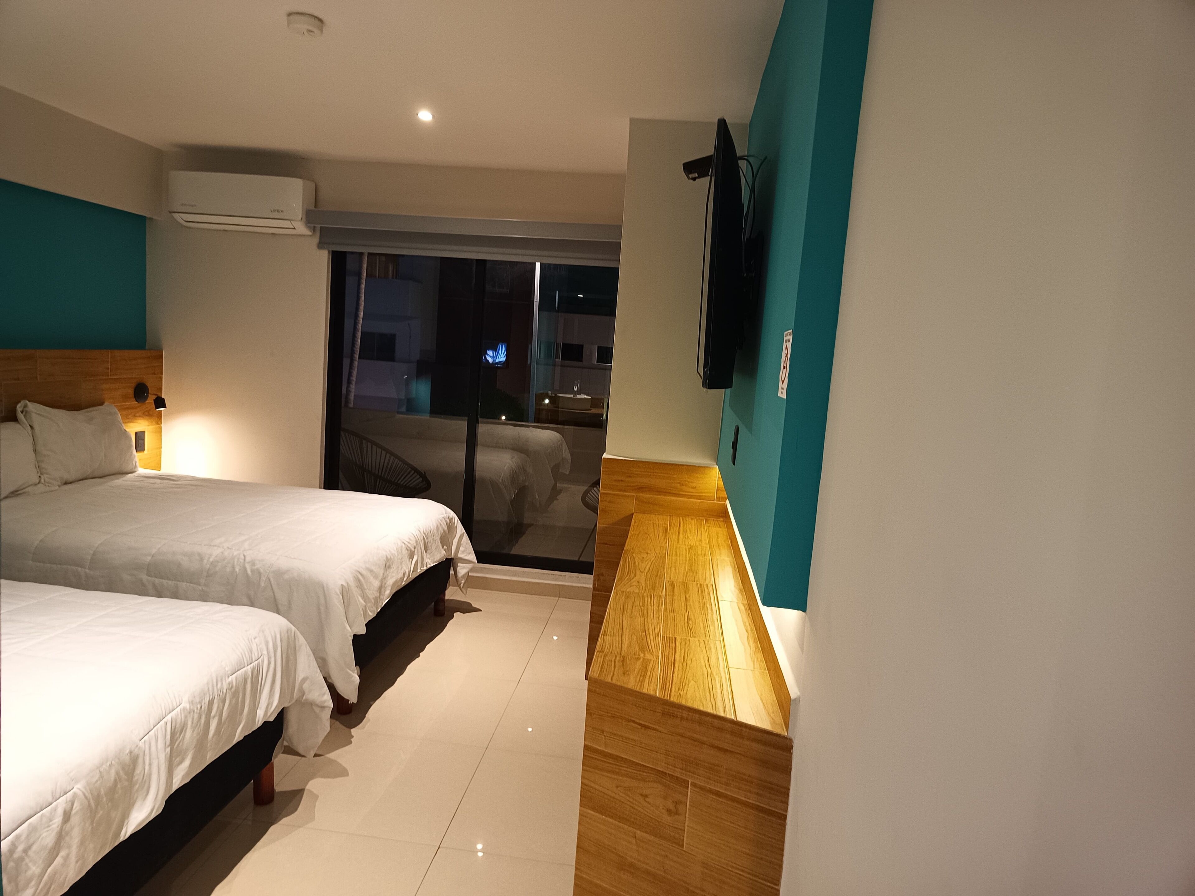 A hotel room with two beds, a TV mounted on the wall, and a balcony with a table and chairs.