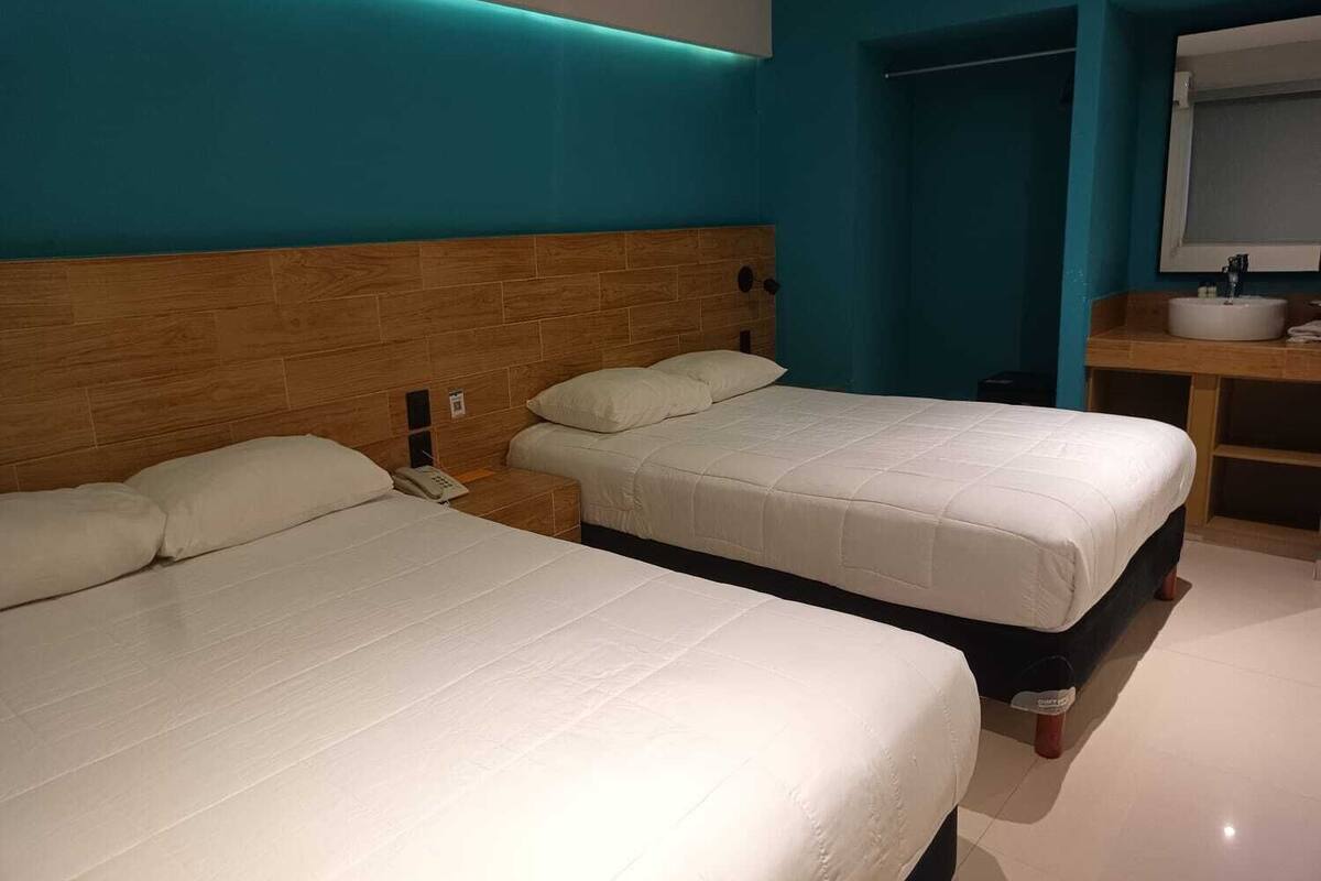 A hotel room with two beds, a wooden headboard, a bathroom with a sink and mirror, and teal walls.