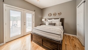 Ein Schlafzimmer mit einem hölzernen Bett, einem Deckenventilator, einem Nachttisch mit Lampe und Blick durch eine Schiebetür.