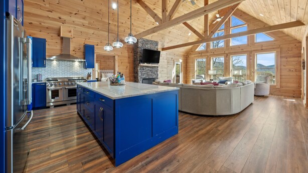 Una cocina amplia con una isla azul, vigas de madera en el techo y grandes ventanas que ofrecen vistas al exterior.