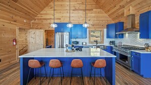 Una cocina moderna con una isla central, armarios azules, electrodomésticos de acero inoxidable y techo de madera.