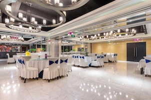 A spacious banquet hall with round tables and chairs, a central column, and a modern ceiling design.