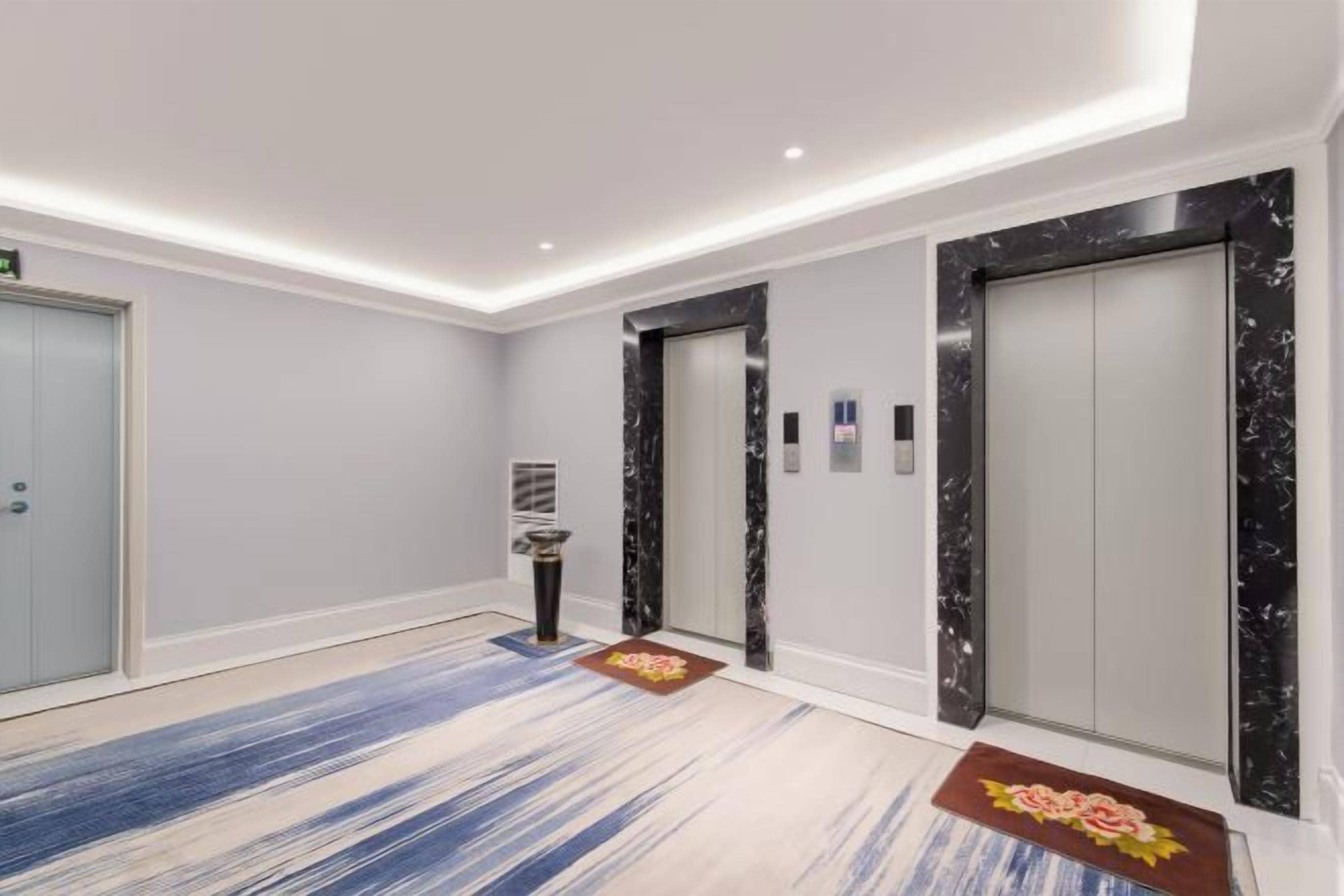 A modern hotel lobby with a marble elevator, a reception desk, and a blue patterned carpet.