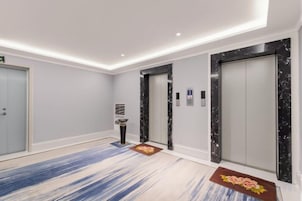 A modern hotel lobby with a marble elevator, a reception desk, and a blue patterned carpet.