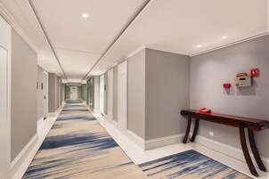 A hotel hallway with a carpeted floor, a bench, and a wall-mounted fire alarm.