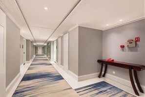 A hotel hallway with a carpeted floor, a bench, and a wall-mounted fire alarm. - Leju Hotel (Jiaozuo Dongfanghong Square) (Jiaozuo)