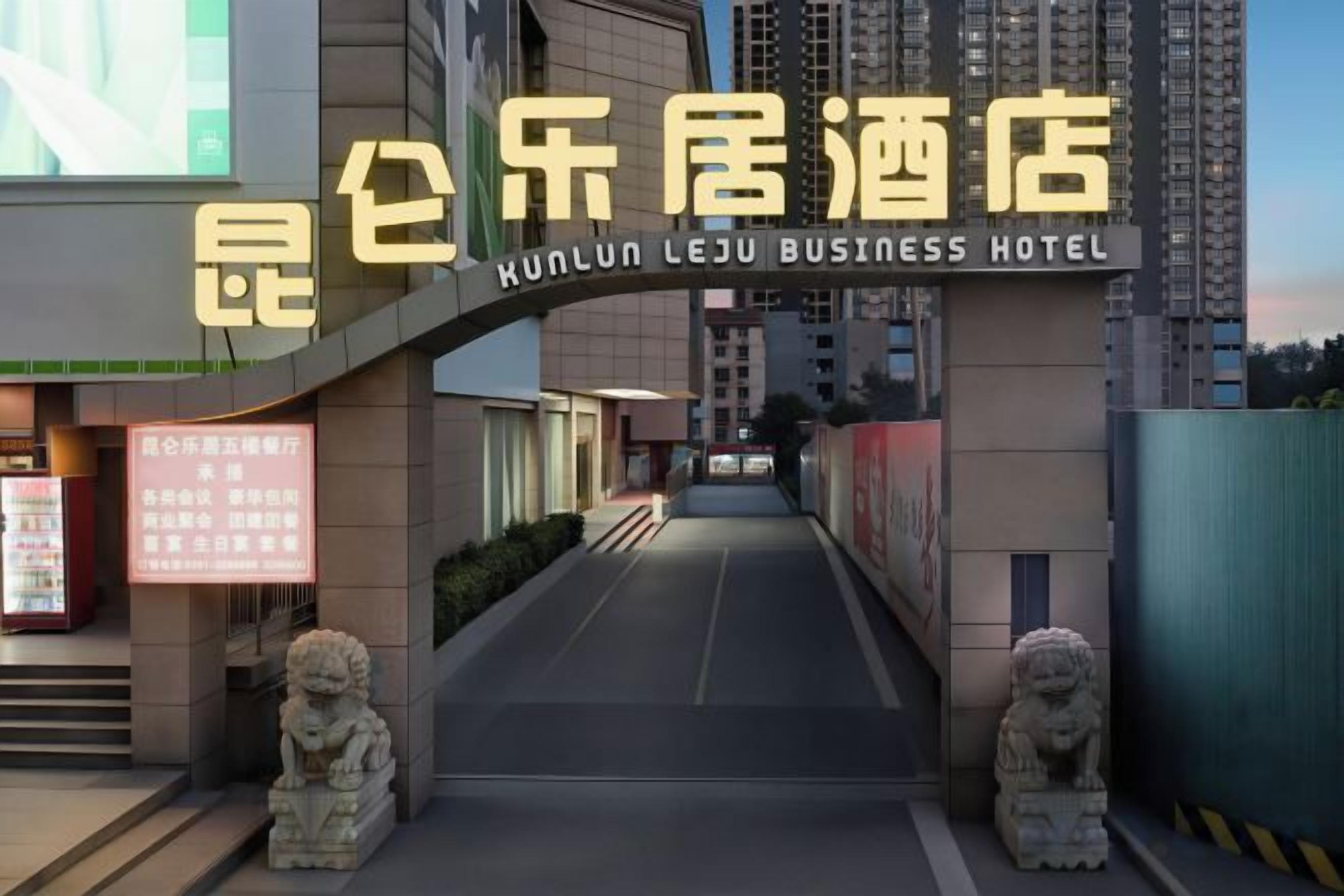 A hotel entrance with a sign for Kunlun Leju Business Hotel, a pathway leading to the entrance, and two stone lion statues on either side.
