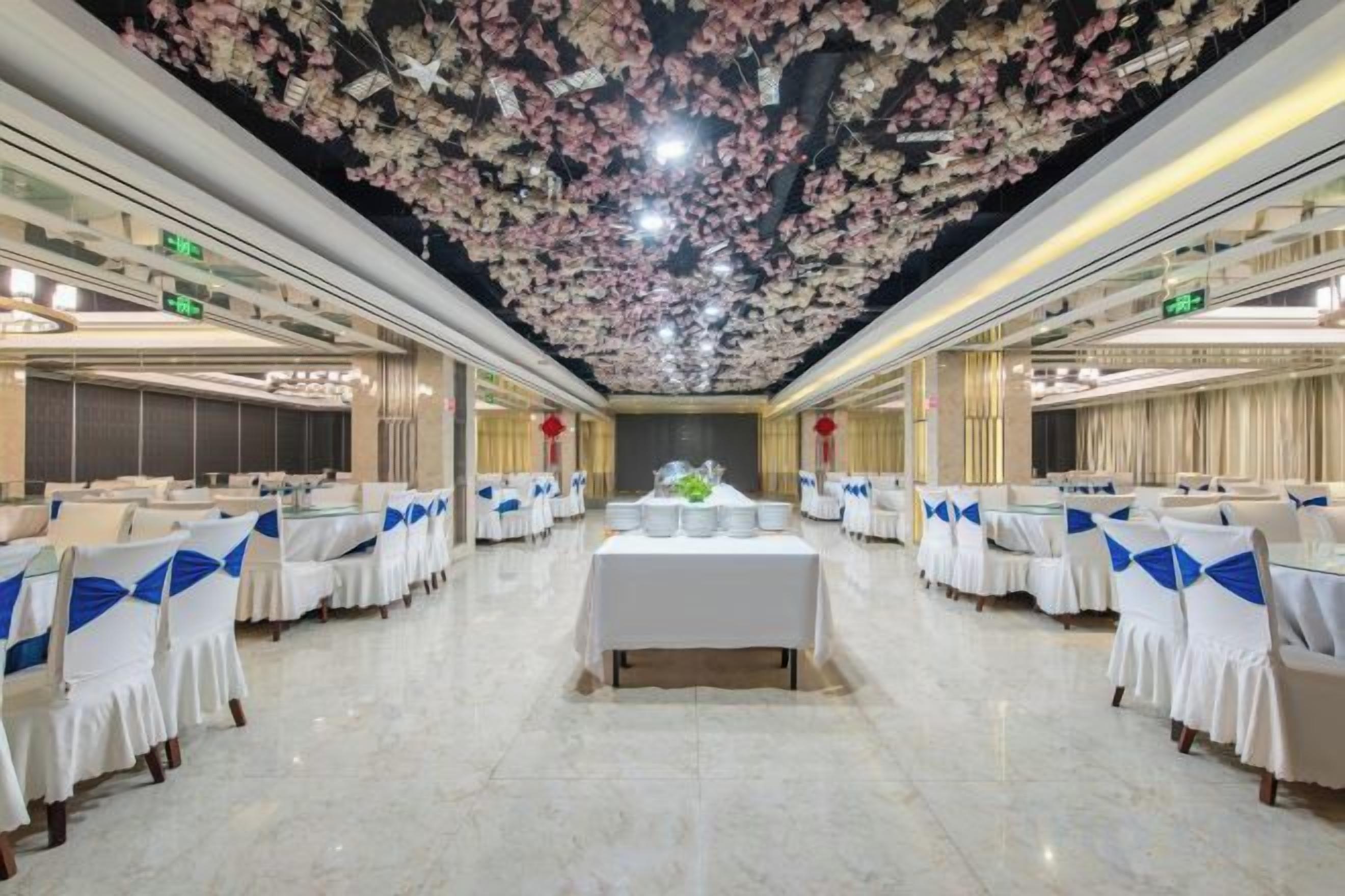 Een feestzaal met aanrijtafels, een decoratief bloemenplafond en een centraal bloemstuk.