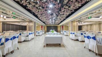 Een feestzaal met aanrijtafels, een decoratief bloemenplafond en een centraal bloemstuk.
