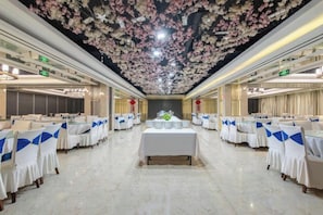 Un salón de banquetes con mesas dispuestas en filas, un diseño floral en el techo y una decoración floral central.