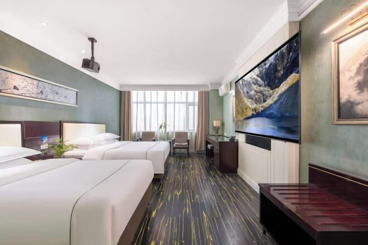 A hotel room with two beds, a desk, a chair, a large painting, and a window.