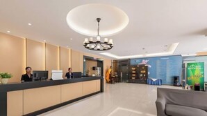 Et hotellets receptionområde med en receptionsdisk, to medarbejdere, en lysekrone, en sofa og en blå væg med tekst.