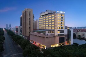 A multi-story hotel with a prominent sign, surrounded by other buildings and a tree-lined street. - Leju Hotel (Jiaozuo Dongfanghong Square) (Jiaozuo)