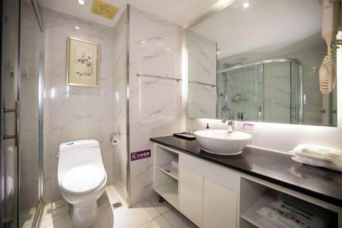 A modern bathroom with a white toilet, a glass shower enclosure, and a large mirror above the sink.
