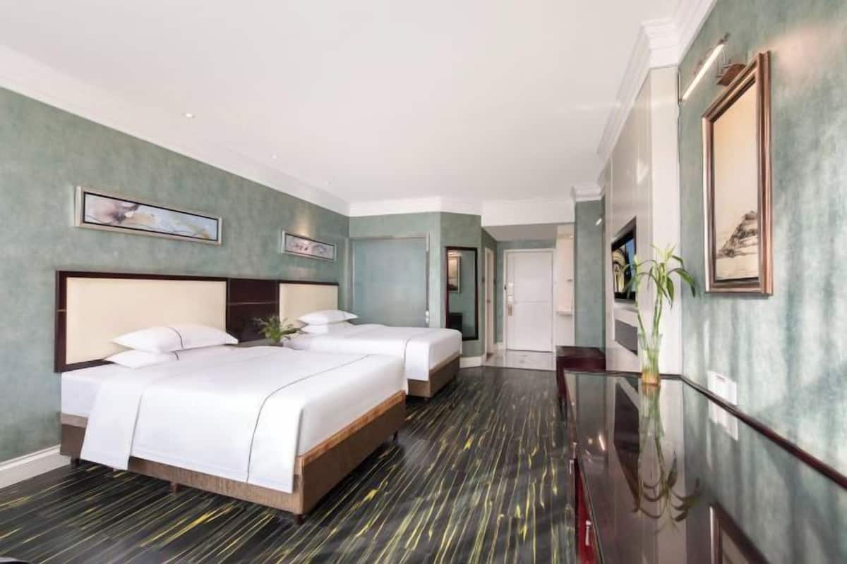 A hotel room with two beds, a large mirror, and a hallway leading to a door.