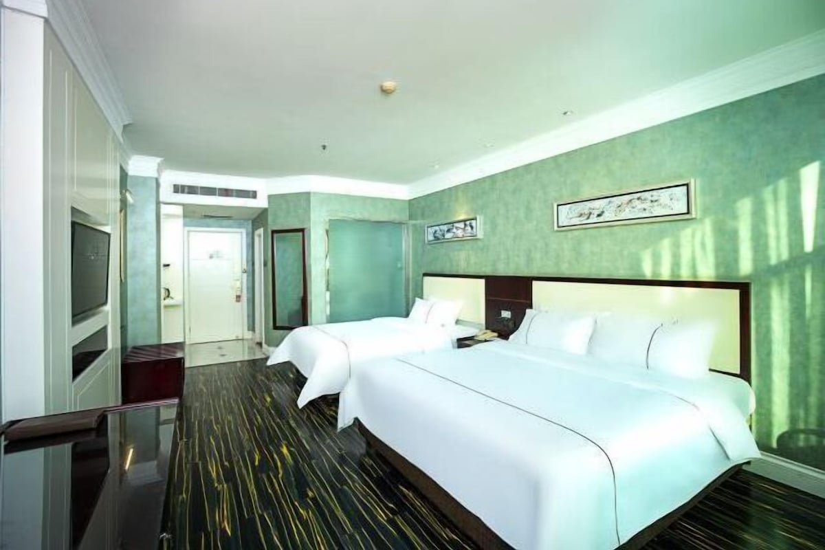 A hotel room with two beds, a flat-screen TV, and a large window.
