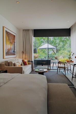 A modern hotel room with a large bed, a sofa, a dining area with a table and chairs, and a balcony with a view of greenery. - Casa Polanco Hotel Boutique (Mexico City)