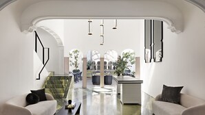 A modern interior with a marble floor, two sofas, a coffee table, and a view of an outdoor patio area with plants and seating. - Casa Polanco Hotel Boutique (Mexico City)