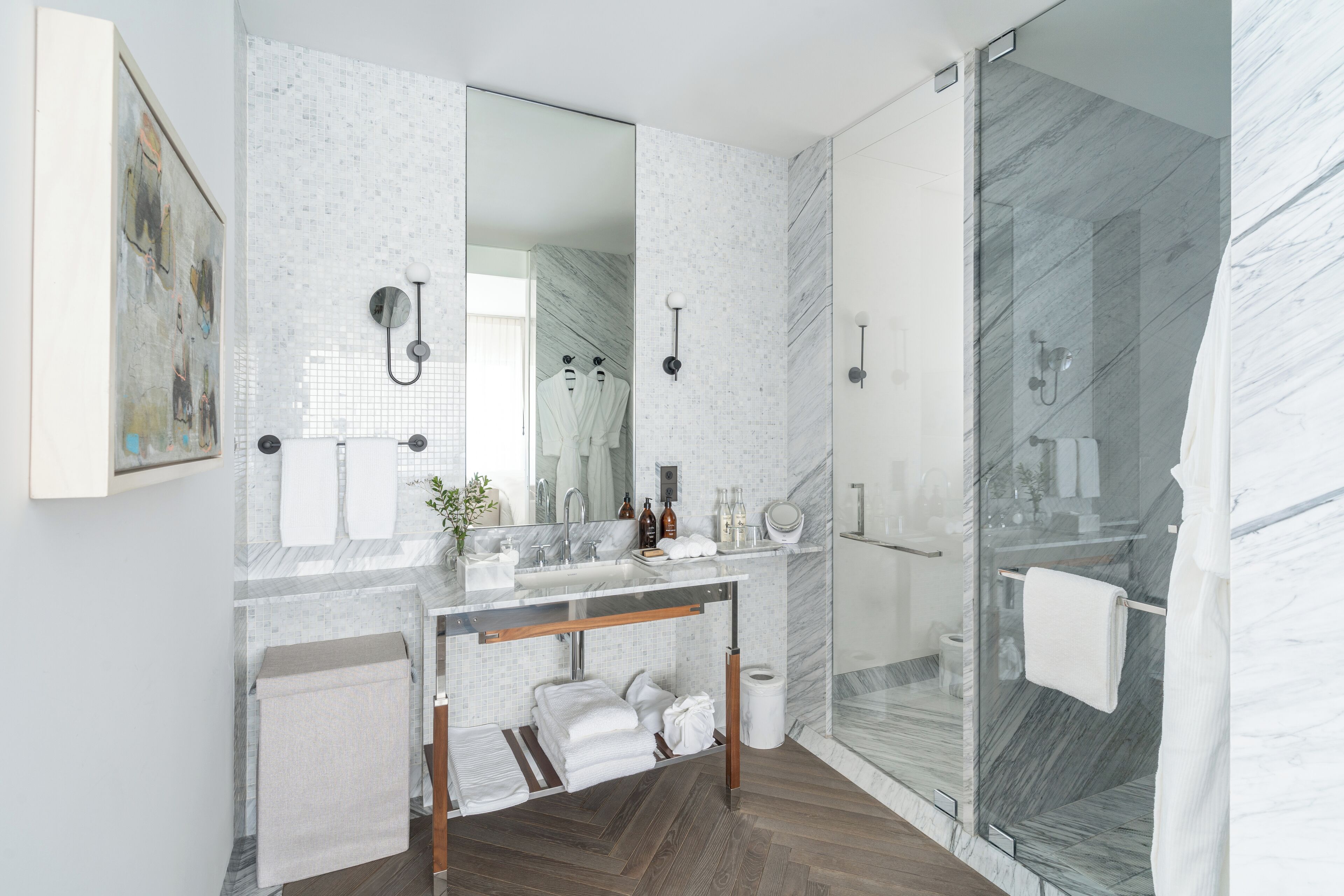 A modern bathroom with a glass shower enclosure, a marble-tiled vanity, and a large mirror.