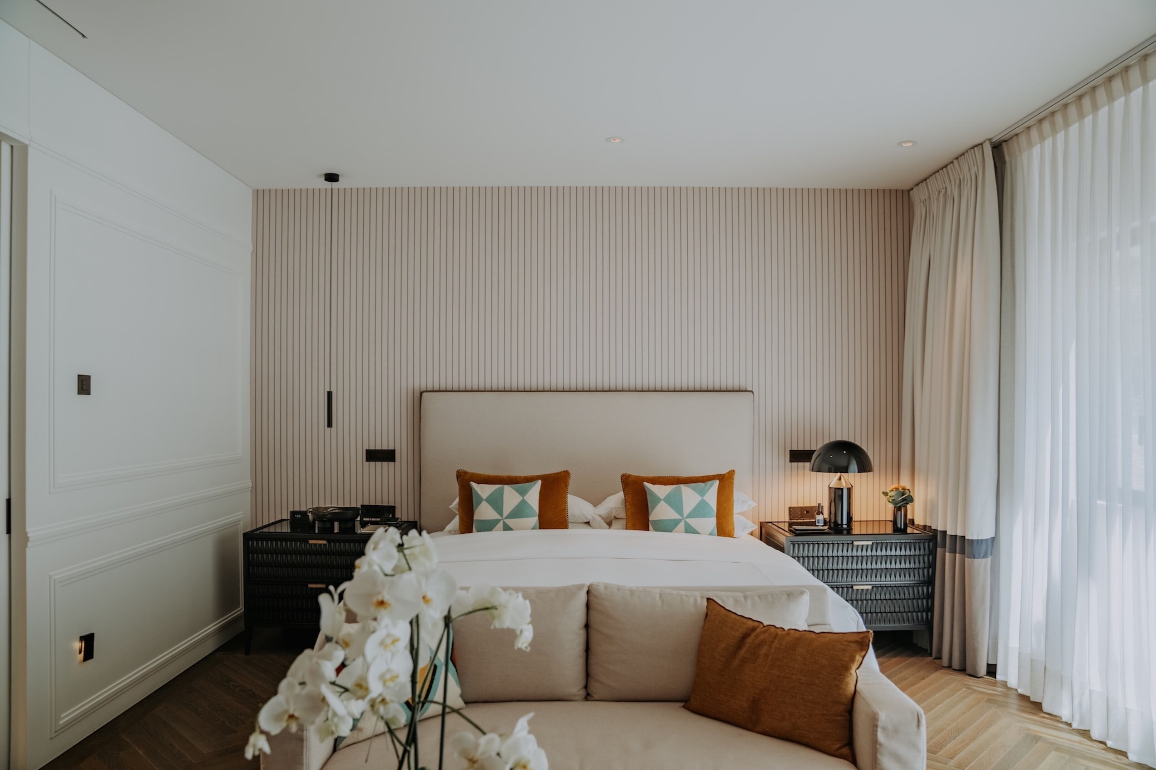 A modern hotel room with a large bed, a bedside table with a lamp, and a nightstand.