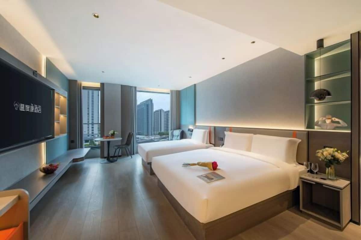 Habitación de hotel con dos camas, televisión, escritorio y vistas a la ciudad.