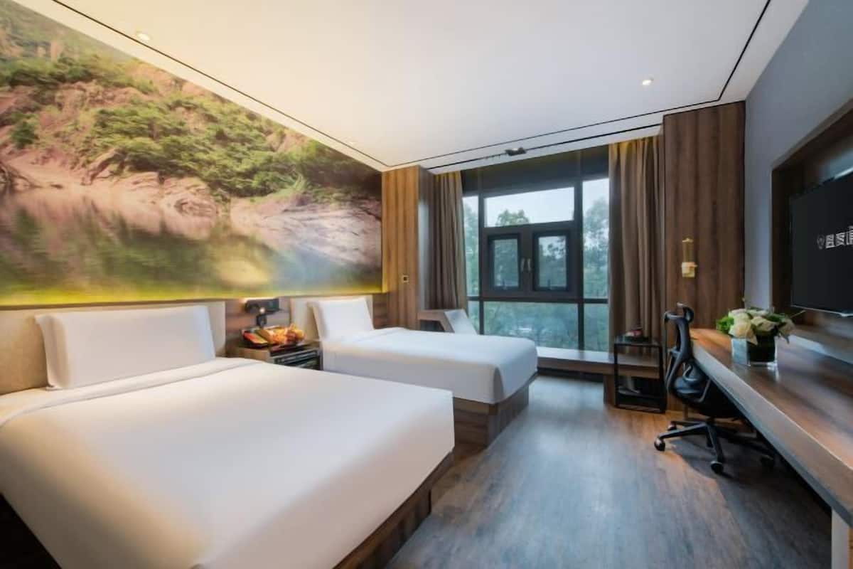 Habitación de hotel con dos camas, un mural grande de un paisaje, un televisor y un escritorio con una silla.