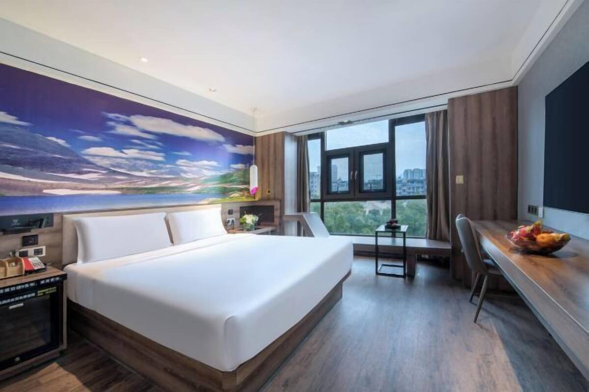Una habitación de hotel moderna con una cama grande, un escritorio y vistas de la ciudad a través de amplios ventanales.