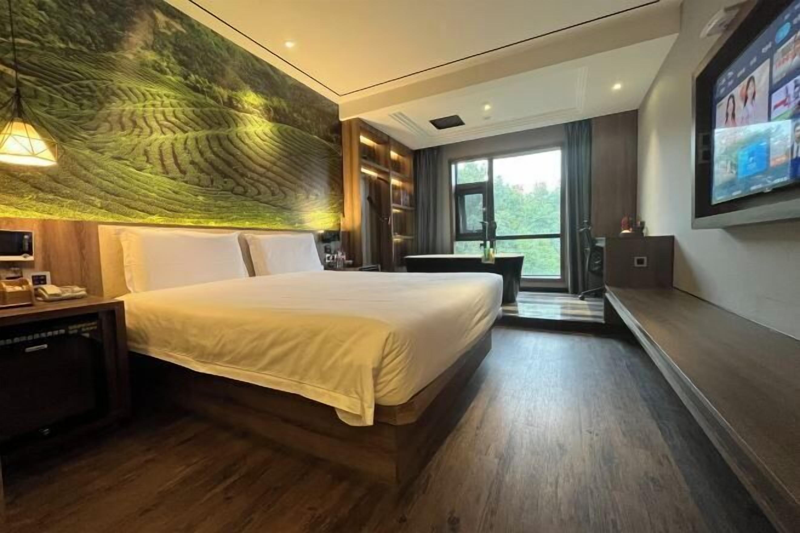 A modern hotel room with a large bed, a television, a desk with a lamp, and a mural on the wall.