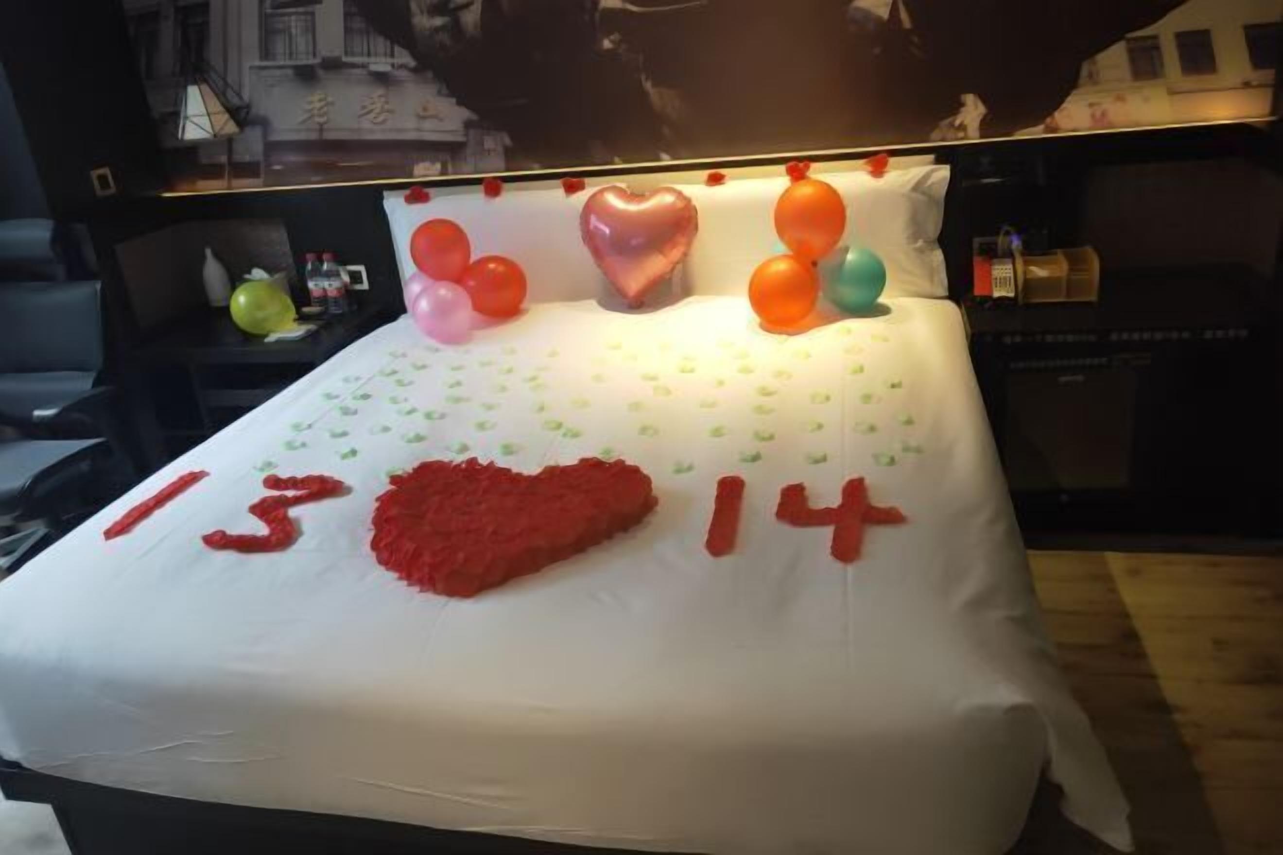 A bed with a white sheet, red heart-shaped decoration, and numbers '13' and '14' on it.