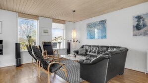 Een moderne woonkamer met een leren zwarte bank, houten stoelen, een salontafel en kunstwerken aan de wanden.