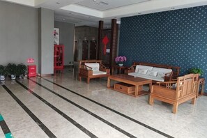 A lobby with a reception desk, wooden furniture, a blue patterned wall, and a tiled floor. - Nanyuan Hotel (Jinsha)