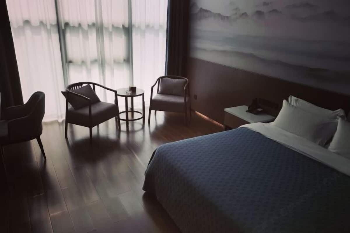 Hotellihuone, jossa on suuri sänky, kaksi nojatuolia, pieni pöytä ja näkymä vuorille ohuiden verhojen läpi.