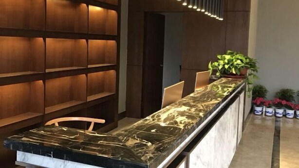 A reception desk with a marble top, wooden paneling on the wall, and a potted plant on the right. - Nanyuan Hotel (Jinsha)