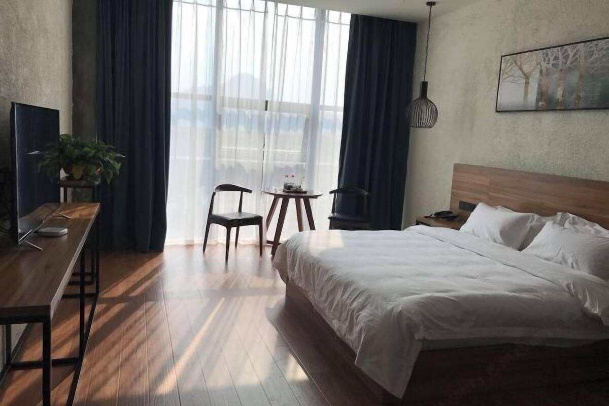 Hotellihuone, jossa on suuri sänky, työpöytä tuolilla, pieni pöytä ja ruukussa oleva kasvi.