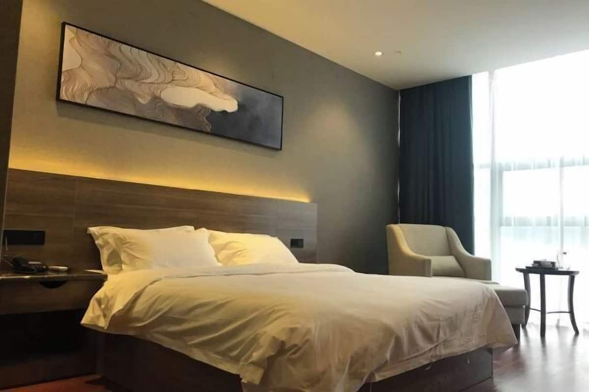 Moderni hotellihuone, jossa on suuri sänky, tuoli, pieni pöytä ja taulu seinällä.