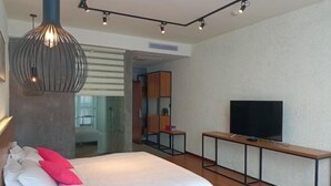 A modern hotel room with a large bed, a TV on a wooden console, and a glass door leading to a bathroom. - Nanyuan Hotel (Jinsha)