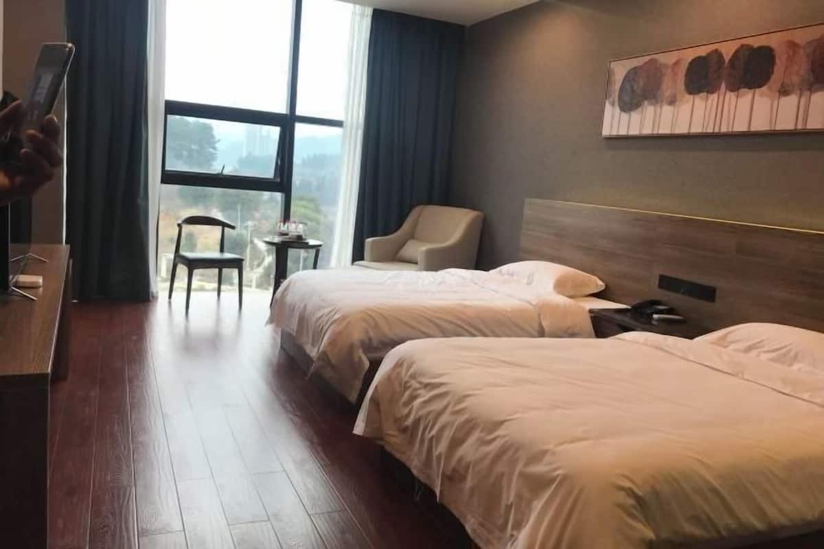 Hotellihuone, jossa on kaksi sänkyä, työpöytä, tuoli ja ikkuna, josta on näkymä.