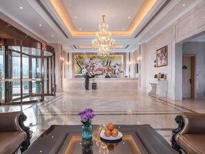 A spacious lobby with a grand chandelier, a reception desk, and a seating area with a vase of flowers. - Vienna International Hotel (Wuxi)