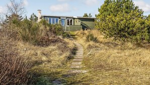A rustic cabin with a stone staircase leading to a wooden door, surrounded by dense shrubbery and trees. - 2 bedroom beautiful home in Rømø (Romo)