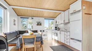 A compact kitchen with white cabinets, a refrigerator, and a dining area with a table and chairs. - 2 bedroom beautiful home in Rømø (Romo)