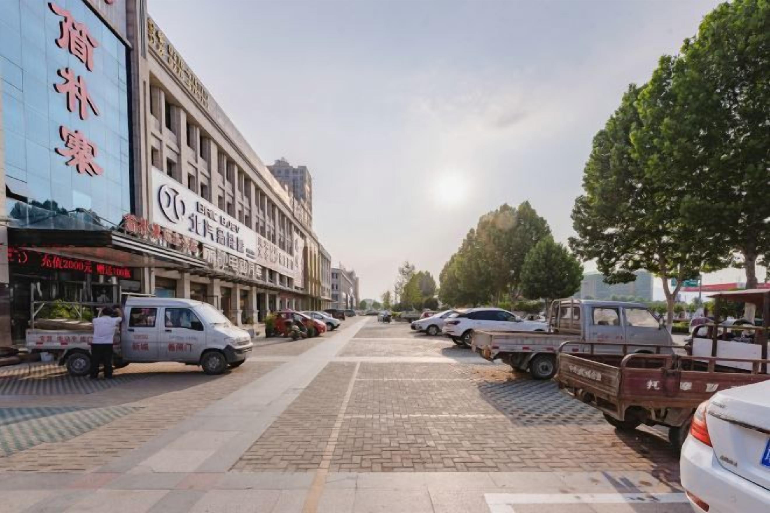 Un carrer amb cotxes aparcats, un edifici amb un rètol i un cel serè.