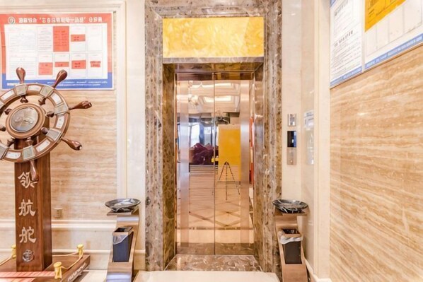 A marble elevator entrance with a ship's wheel decoration, a yellow sign above, and a poster on the wall. - Shangcheng lijingyuan Hotel (Shangcheng)