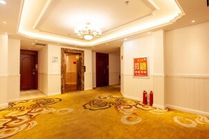 A hotel corridor with a patterned carpet, a chandelier, and fire extinguishers.