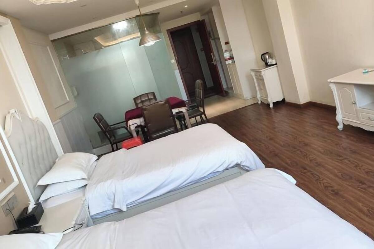 Habitación de hotel con dos camas, zona de comedor con sillas, una pequeña mesa y una kitchenette.