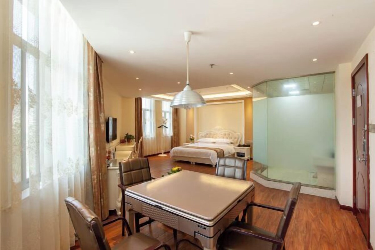A hotel room with a bed, bedside table, lamp, and a dining area with chairs and a table.
