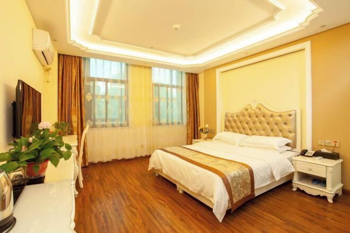 Habitación de hotel con una cama grande, una mesita de noche, un televisor y una ventana con cortinas.